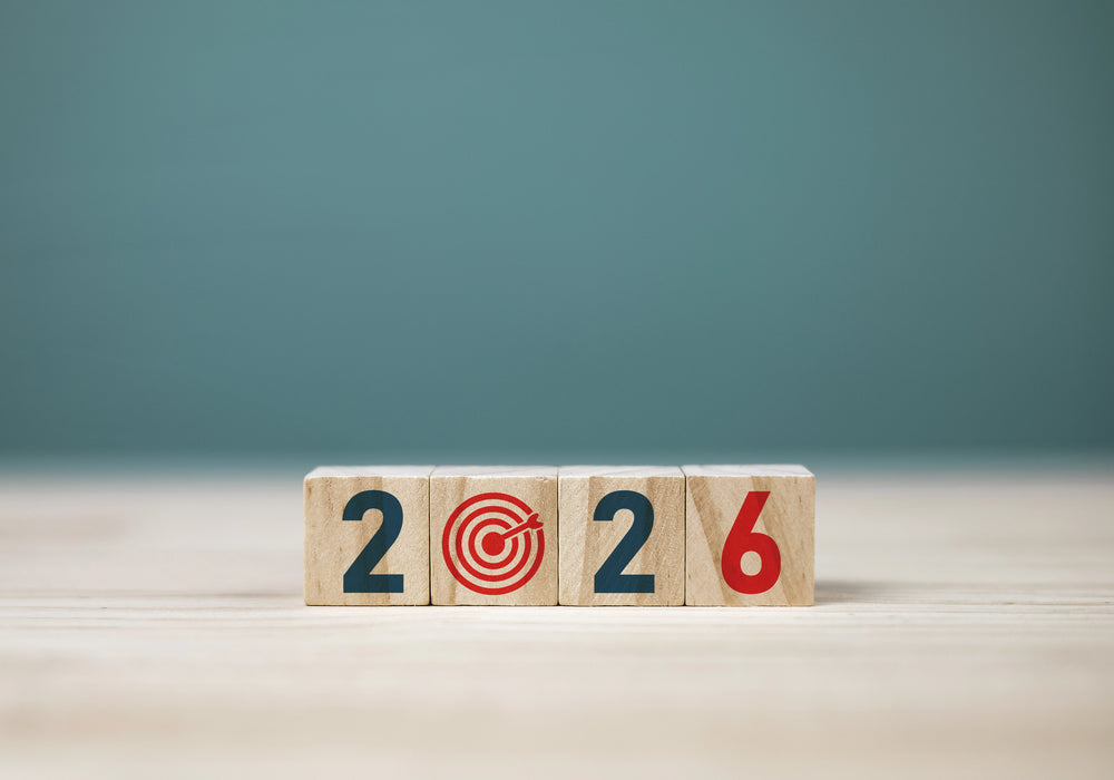 Wooden blocks display 2026 with a bullseye replacing the zero, arranged on a light wood tabletop against a muted teal background.