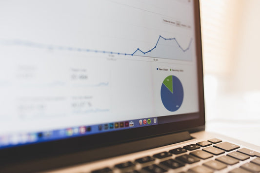 Laptop displaying analytics dashboard with line graph and pie chart, shown as a close-up over the keyboard in a bright workspace.